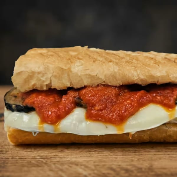 Close-up of an eggplant parmesan sandwich on a baguette, with melted cheese and red sauce.