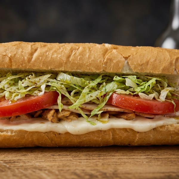Close-up of a chicken sub sandwich with melted cheese, tomatoes, and lettuce on a wooden surface.